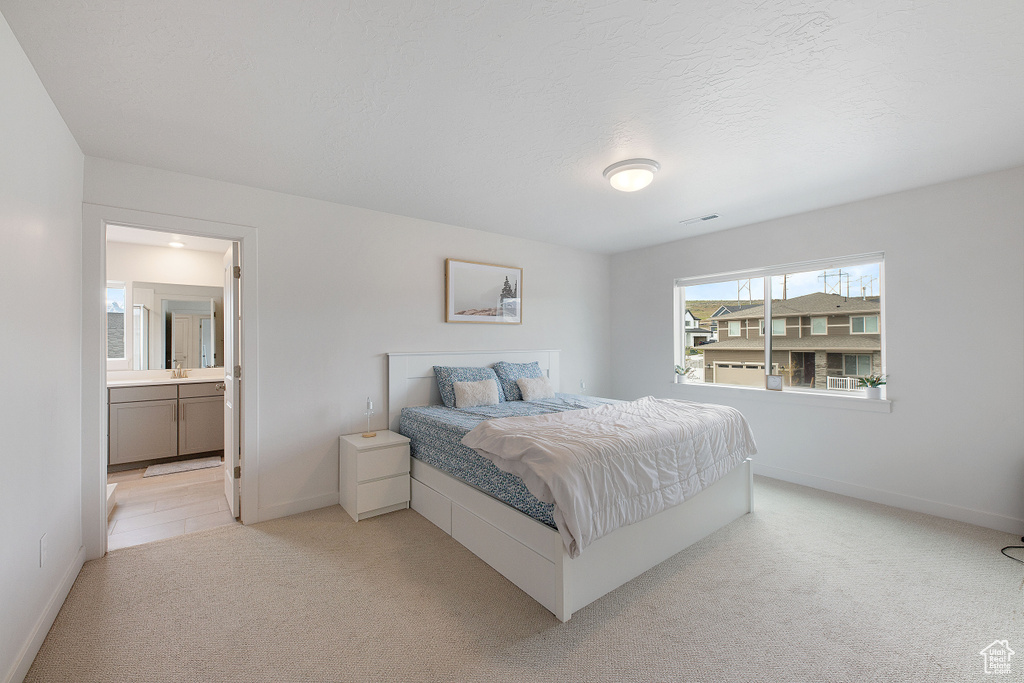 Bedroom featuring light carpet, baseboards, and ensuite bathroom