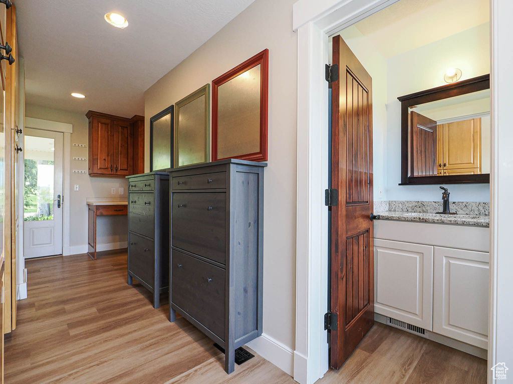 Corridor featuring light wood-style floors, baseboards, recessed lighting, and a sink
