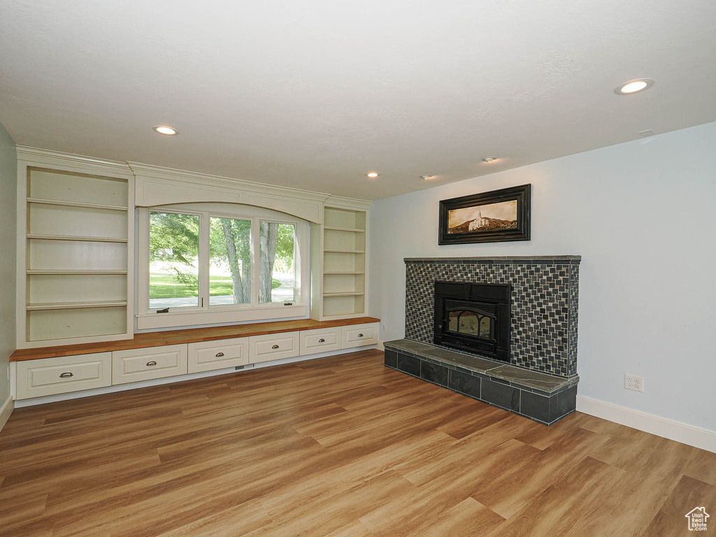 Unfurnished living room with light wood-style floors, baseboards, a tiled fireplace, recessed lighting, and built in shelves