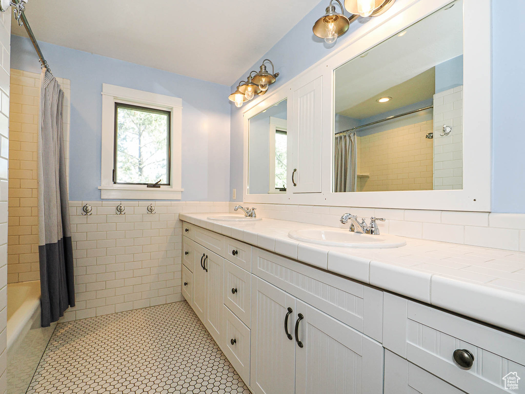 Bathroom featuring double vanity, tile patterned flooring, a wainscoted wall, shower / bath combo with shower curtain, and tile walls