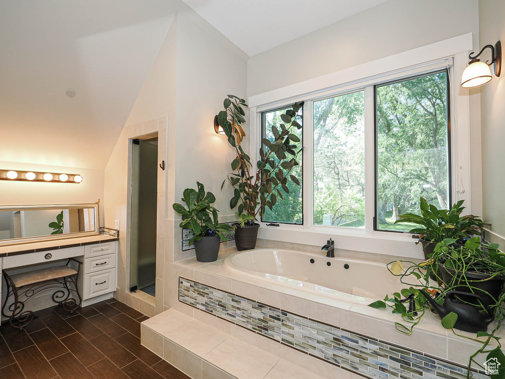 Full bath featuring plenty of natural light, a bath, vanity, lofted ceiling, and a shower stall