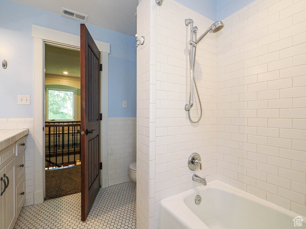 Bathroom with tile walls, toilet, shower / washtub combination, tile patterned floors, and a wainscoted wall