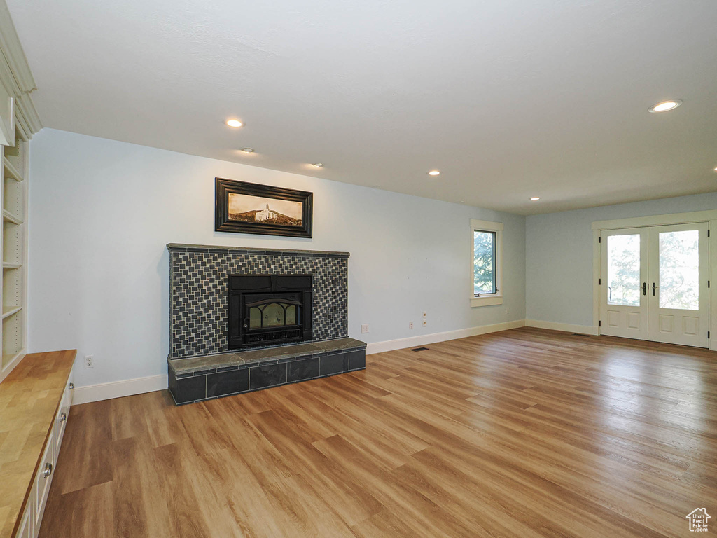 Unfurnished living room featuring light wood-style flooring, baseboards, recessed lighting, a fireplace, and french doors