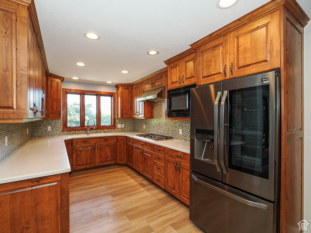 Kitchen with stainless steel fridge with ice dispenser, under cabinet range hood, black microwave, brown cabinets, and light wood finished floors
