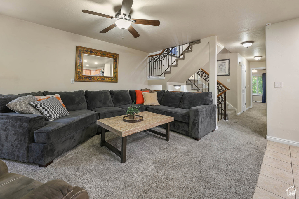 Living area with a ceiling fan, stairway, light tile patterned floors, baseboards, and light colored carpet