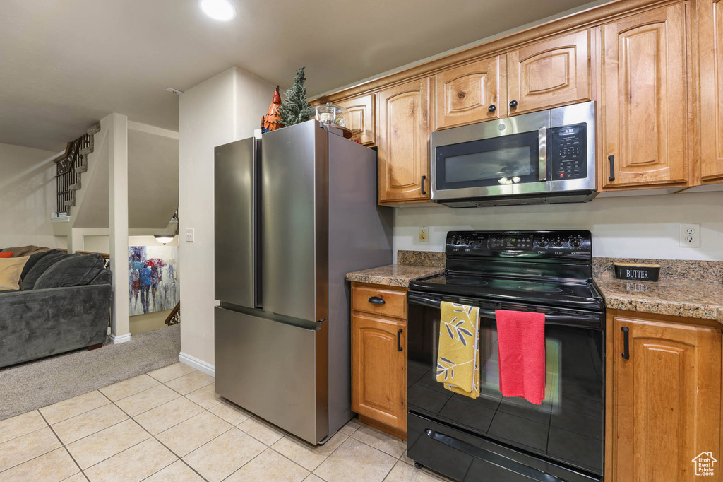 Kitchen with appliances with stainless steel finishes, open floor plan, light tile patterned flooring, and brown cabinets