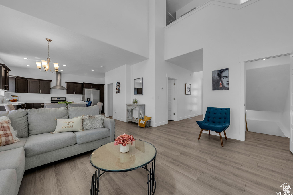 Living area featuring a chandelier, light wood-type flooring, recessed lighting, baseboards, and a high ceiling