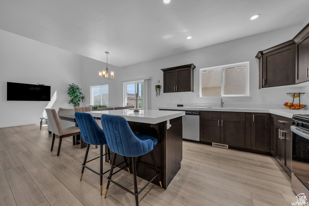 Kitchen featuring appliances with stainless steel finishes, a chandelier, a kitchen island, dark brown cabinets, and a breakfast bar