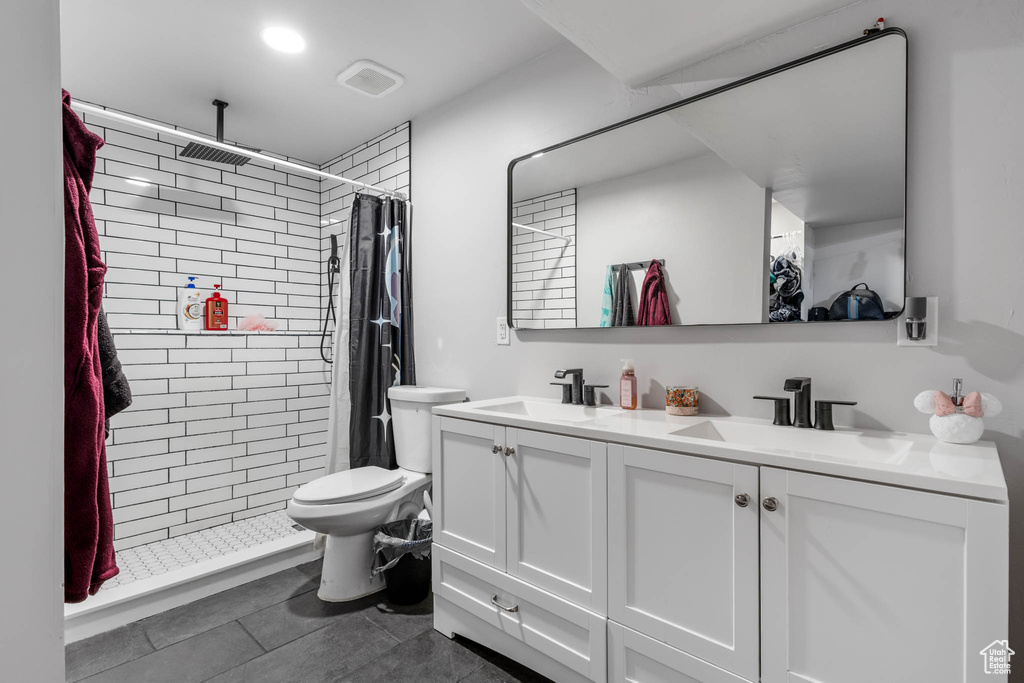 Full bath with double vanity, tiled shower, tile patterned floors, and toilet