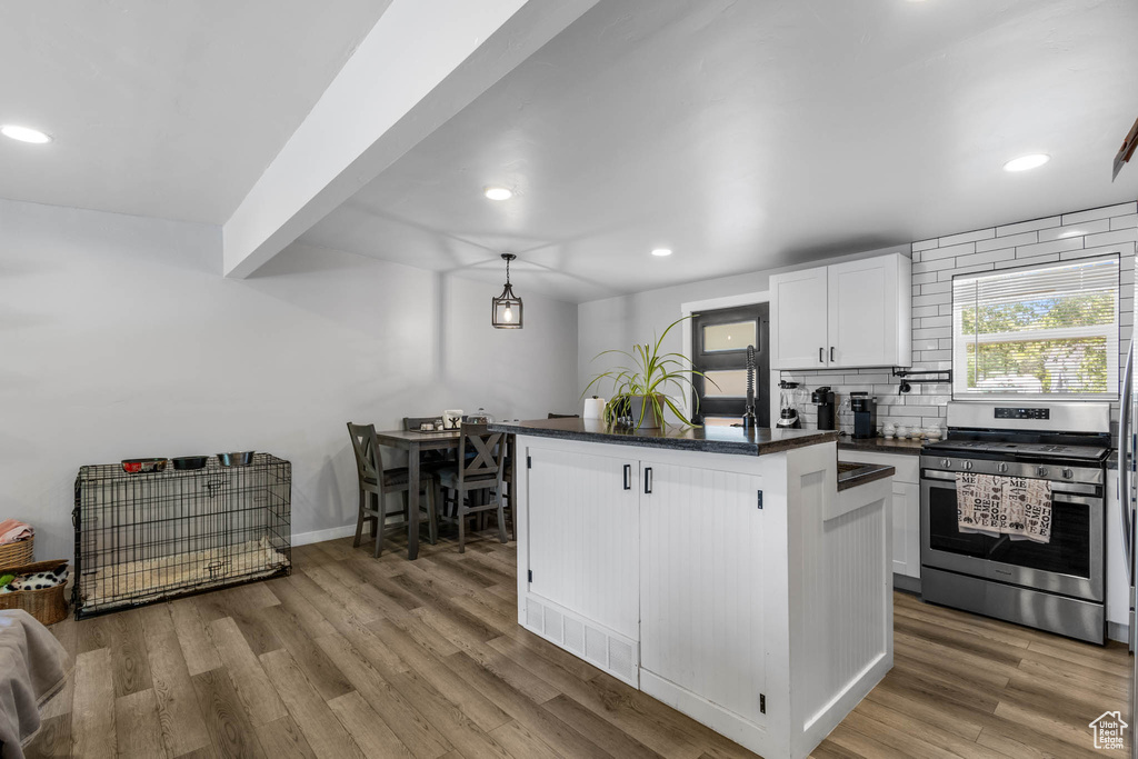 Kitchen with stainless steel gas range, backsplash, recessed lighting, white cabinets, and light wood-style floors