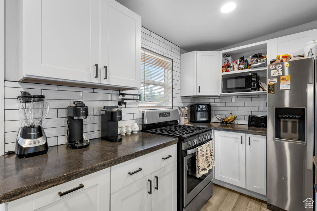 Kitchen featuring stainless steel appliances, backsplash, white cabinetry, and dark stone countertops