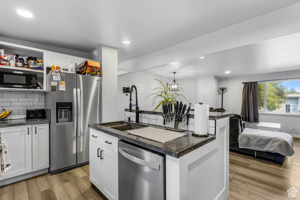 Kitchen with stainless steel appliances, dark countertops, light wood-style floors, white cabinets, and recessed lighting