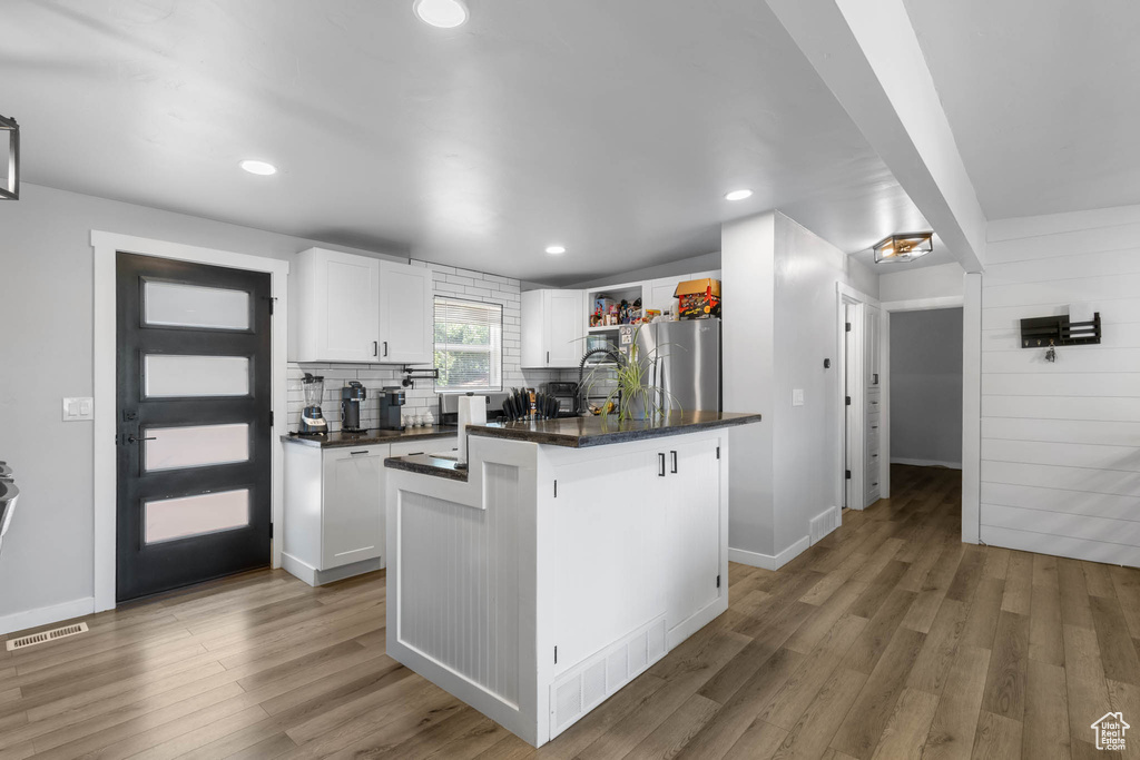 Kitchen with freestanding refrigerator, dark countertops, white cabinetry, light wood-type flooring, and decorative backsplash