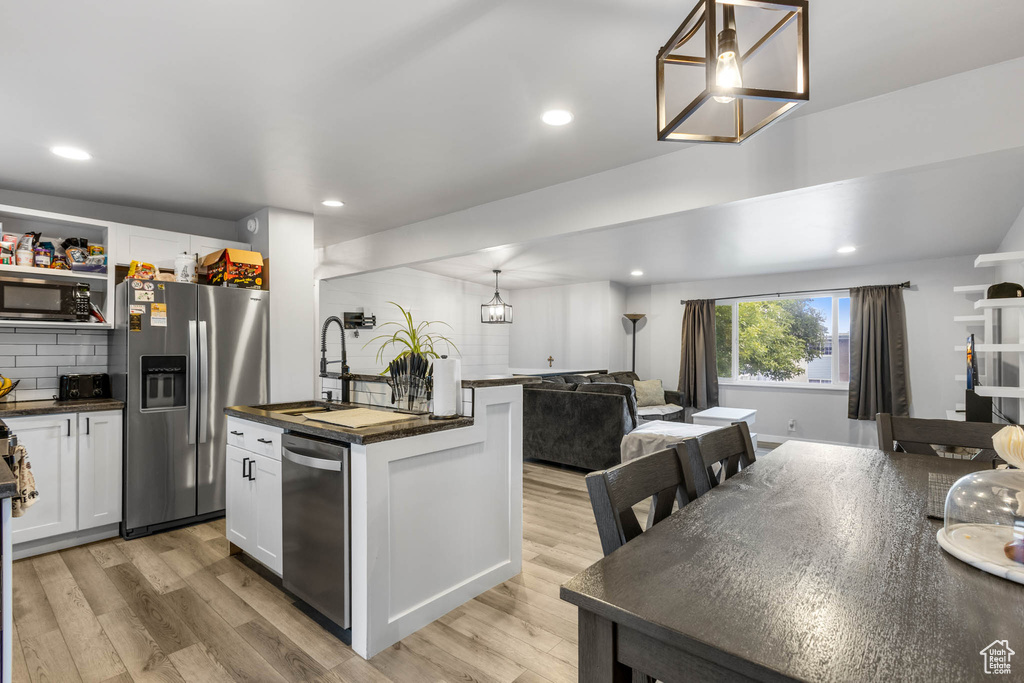 Kitchen with appliances with stainless steel finishes, open floor plan, light wood finished floors, a sink, and a chandelier
