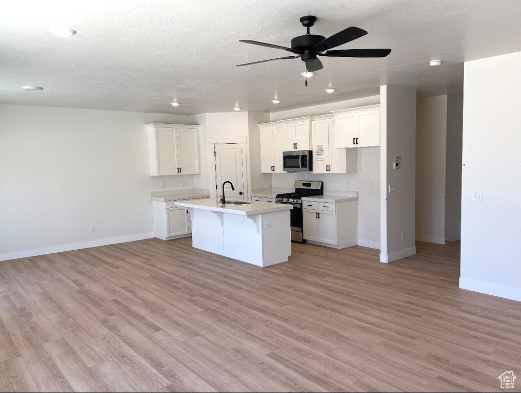 Kitchen with stainless steel appliances, baseboards, a sink, light wood-type flooring, and a kitchen island with sink