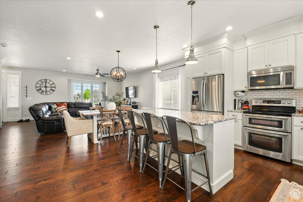 Kitchen featuring appliances with stainless steel finishes, open floor plan, decorative backsplash, light stone countertops, and a kitchen breakfast bar