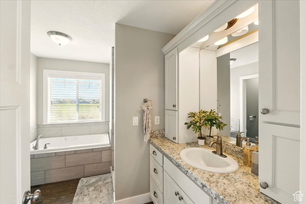 Full bath with vanity, a garden tub, and wood finished floors