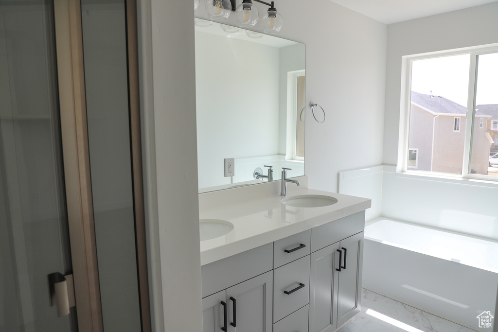 Full bathroom with double vanity, marble finish flooring, and a bath