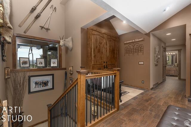 Hall with an upstairs landing, lofted ceiling, wood finished floors, and baseboards