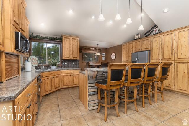 Kitchen with appliances with stainless steel finishes, backsplash, light tile patterned floors, a kitchen bar, and lofted ceiling