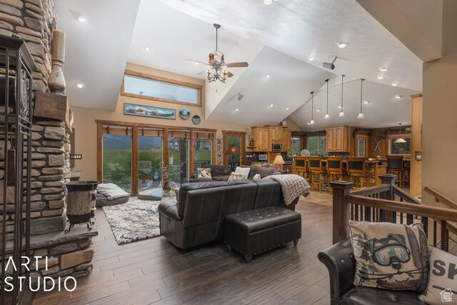 Living area featuring ceiling fan, wood finished floors, vaulted ceiling, and a stone fireplace