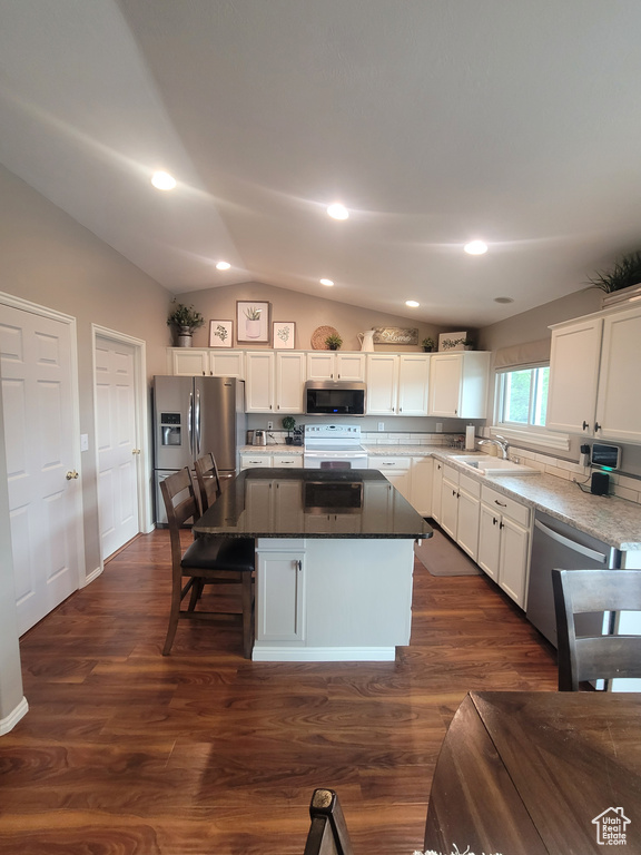 Kitchen featuring appliances with stainless steel finishes, lofted ceiling, a kitchen island, white cabinets, and dark wood-type flooring