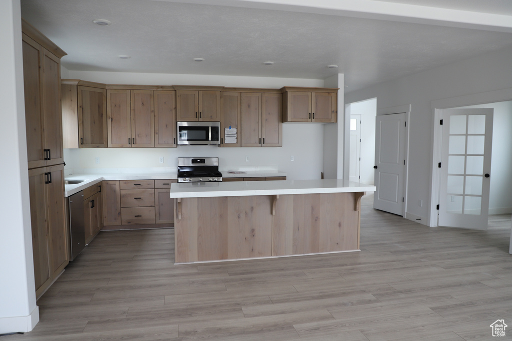 Kitchen featuring appliances with stainless steel finishes, a center island, light countertops, light wood-type flooring, and a kitchen breakfast bar