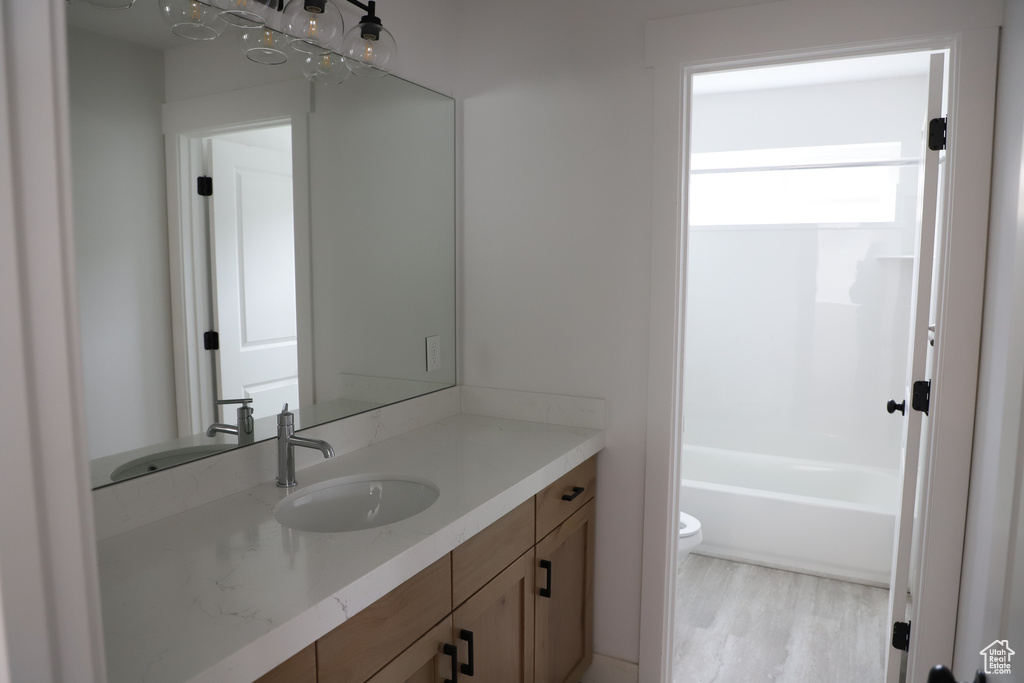Bathroom featuring toilet, vanity, wood finished floors, and washtub / shower combination