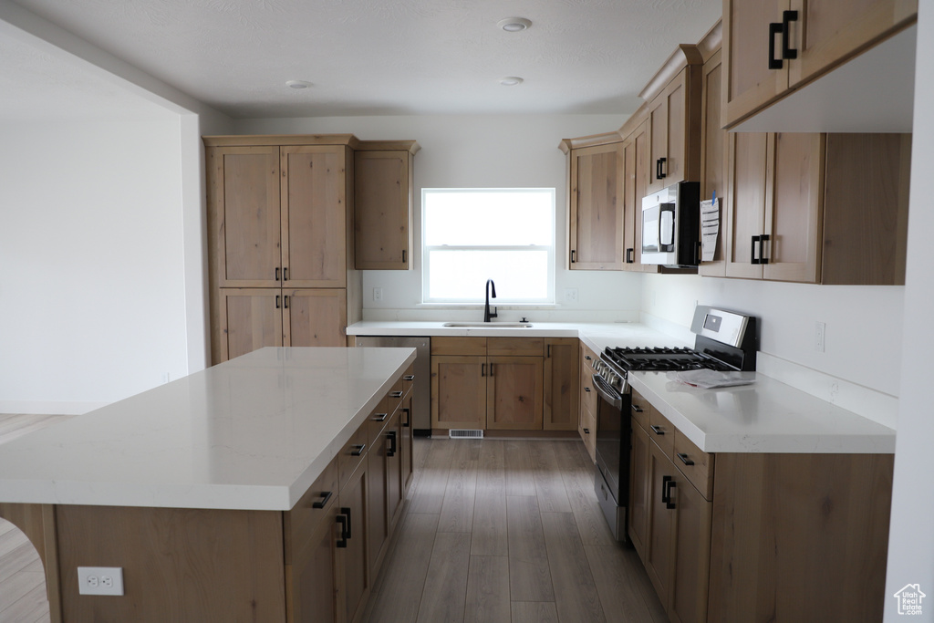 Kitchen featuring stainless steel appliances, a sink, a kitchen island, light wood-style floors, and light brown cabinets