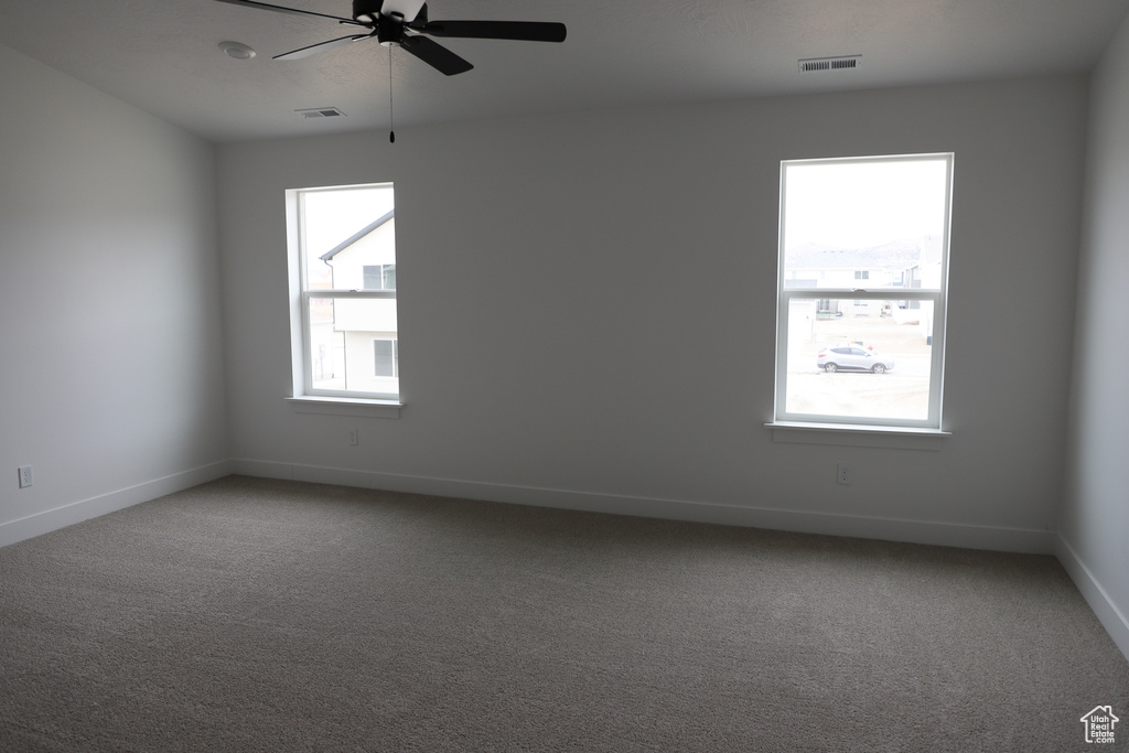 Carpeted spare room featuring a ceiling fan and baseboards