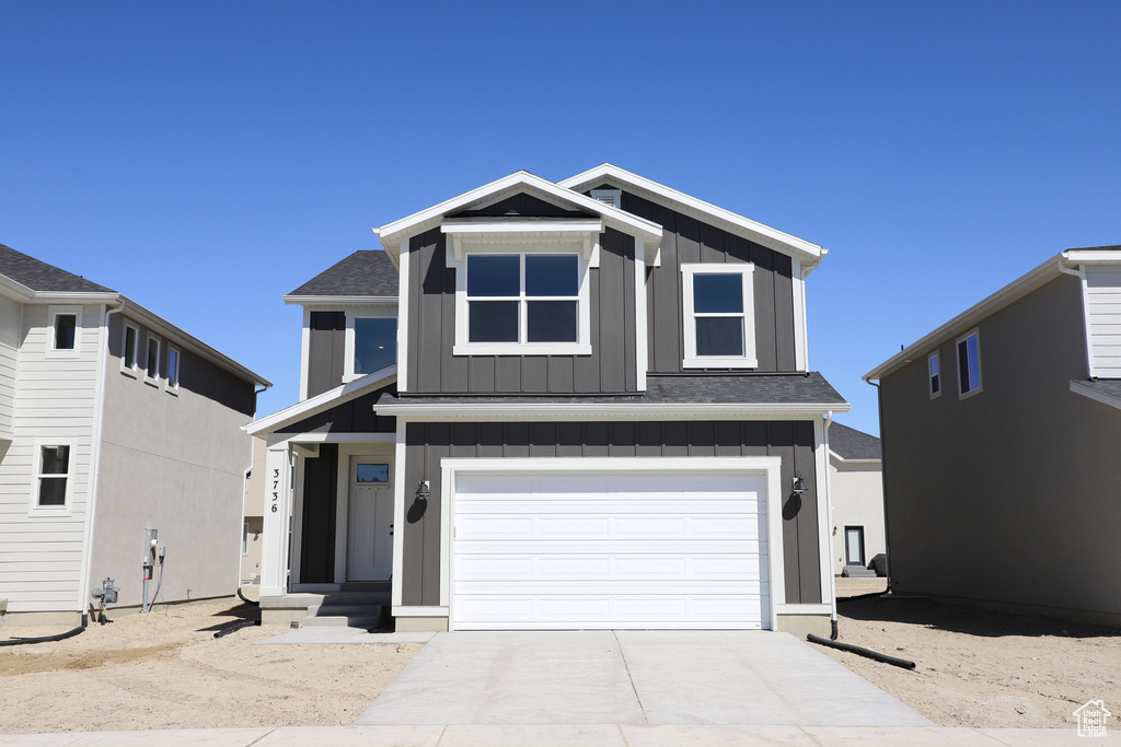 View of front facade with board and batten siding, a garage, driveway, and a shingled roof