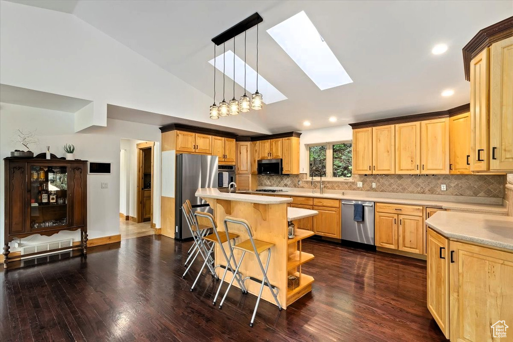 Kitchen with appliances with stainless steel finishes, a skylight, light countertops, vaulted ceiling, and light brown cabinets