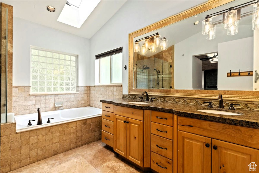 Bathroom featuring a skylight, lofted ceiling, a shower stall, double vanity, and a garden tub
