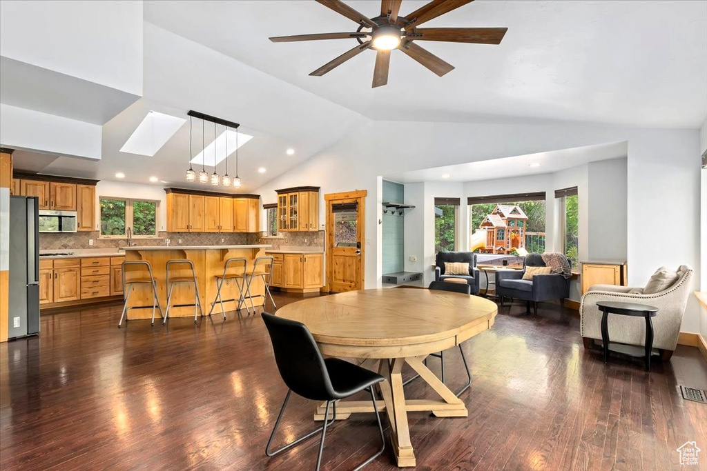Dining space with lofted ceiling, dark wood-type flooring, a skylight, a ceiling fan, and recessed lighting
