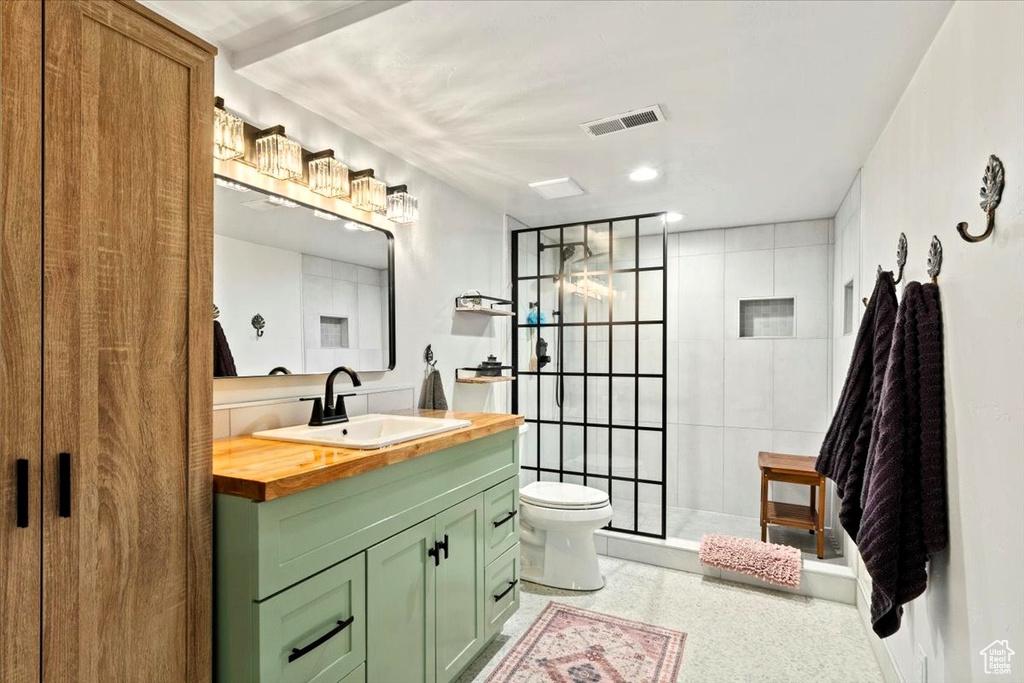 Full bathroom featuring vanity, toilet, tiled shower, and speckle patterned floor