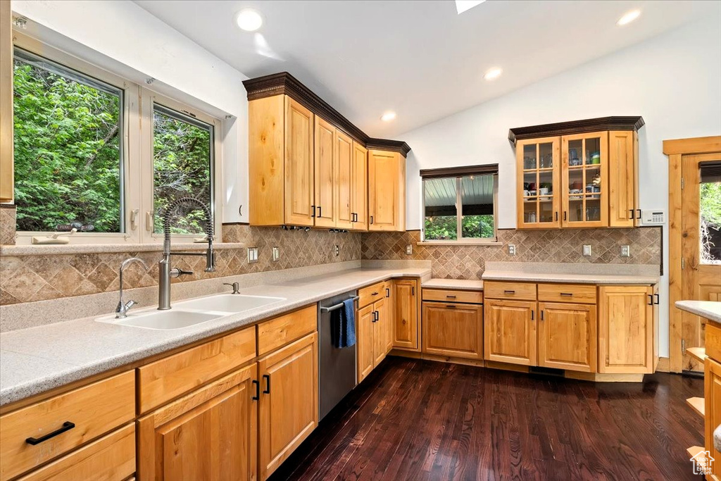Kitchen with lofted ceiling, dark wood-style floors, stainless steel dishwasher, light countertops, and backsplash