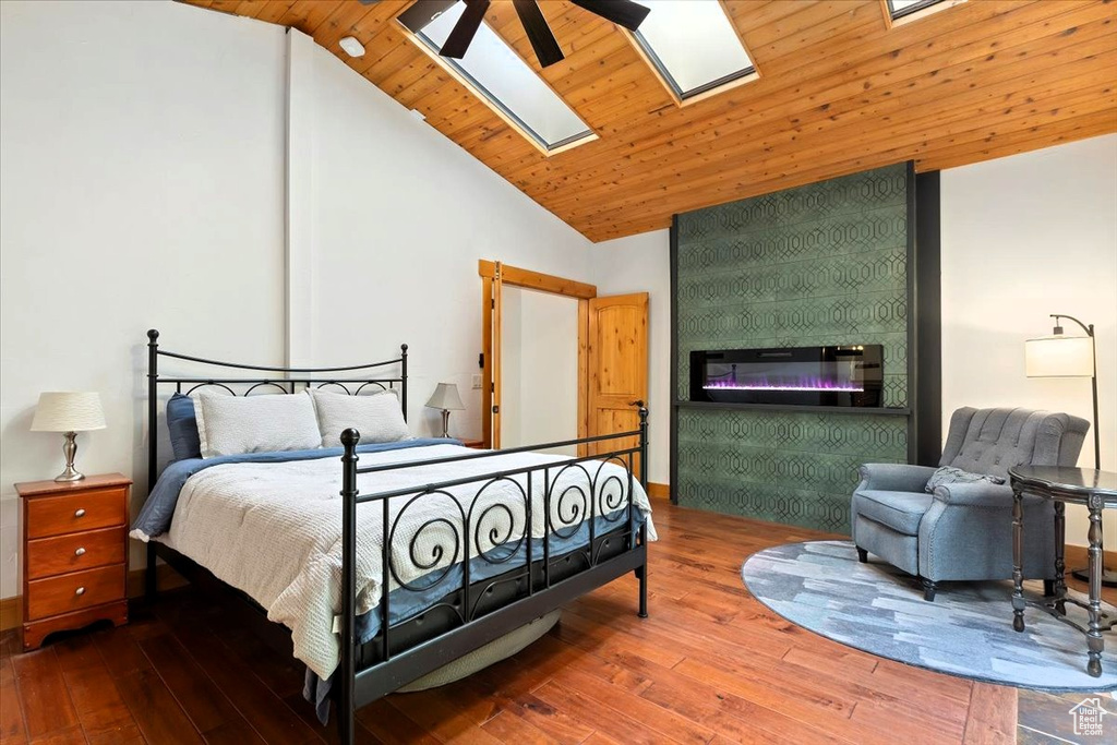 Bedroom with hardwood / wood-style floors, a skylight, a large fireplace, high vaulted ceiling, and wood ceiling
