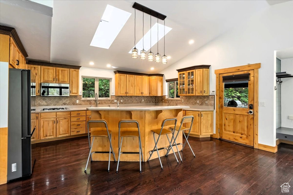 Kitchen featuring appliances with stainless steel finishes, a skylight, a kitchen bar, light countertops, and vaulted ceiling