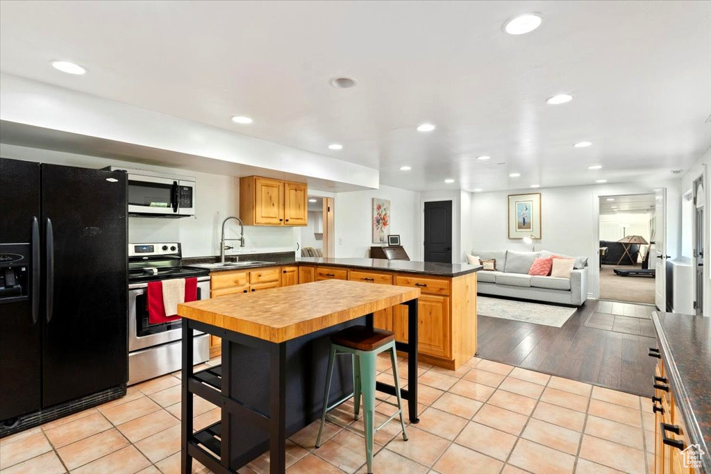 Kitchen featuring stainless steel range with electric stovetop, black refrigerator with ice dispenser, a sink, a peninsula, and recessed lighting
