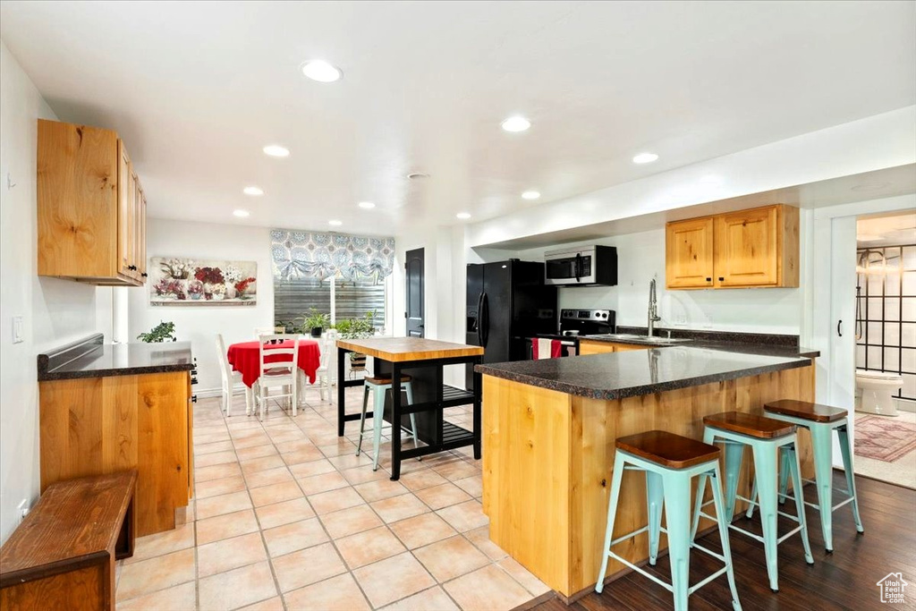 Kitchen featuring stainless steel appliances, a sink, a breakfast bar, dark countertops, and recessed lighting