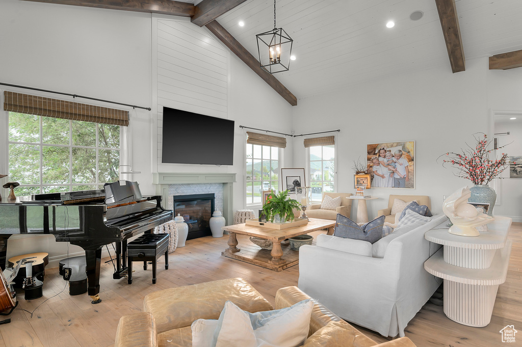 Living area featuring beamed ceiling, hardwood / wood-style flooring, high vaulted ceiling, a glass covered fireplace, and a chandelier