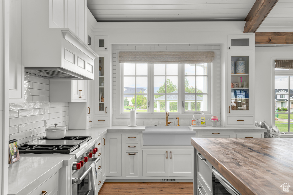 Kitchen featuring butcher block counters, high end stainless steel range, a sink, white cabinetry, and beamed ceiling