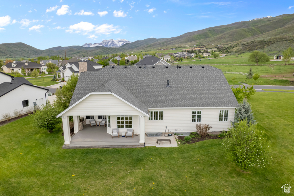 Back of property featuring a mountain view, a patio, roof with shingles, and a yard