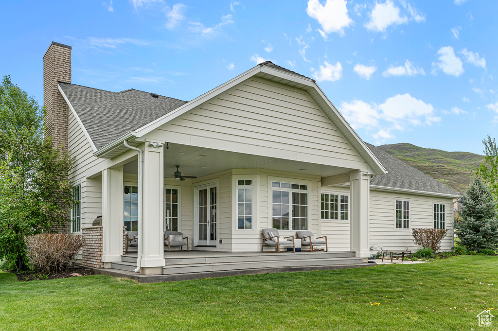 Back of house featuring ceiling fan, a lawn, a chimney, roof with shingles, and a mountain view