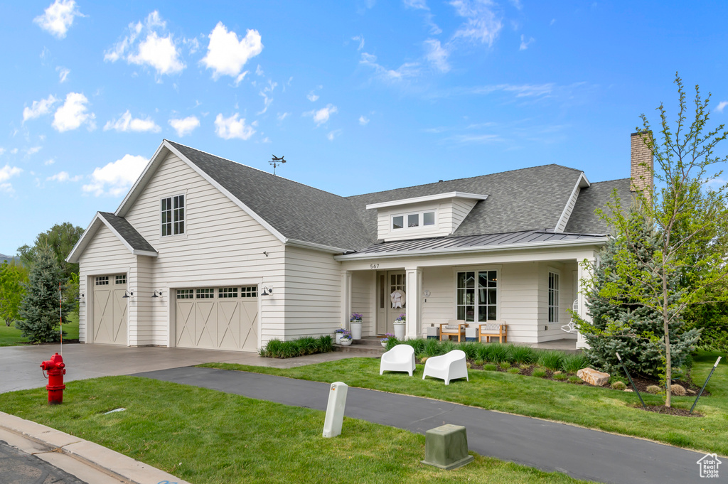 View of front of home with a standing seam roof, concrete driveway, a porch, a front lawn, and roof with shingles