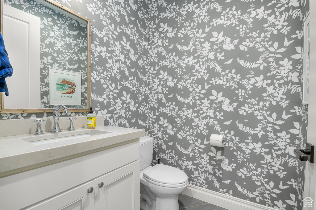 Half bathroom featuring wallpapered walls, toilet, tile patterned flooring, vanity, and baseboards