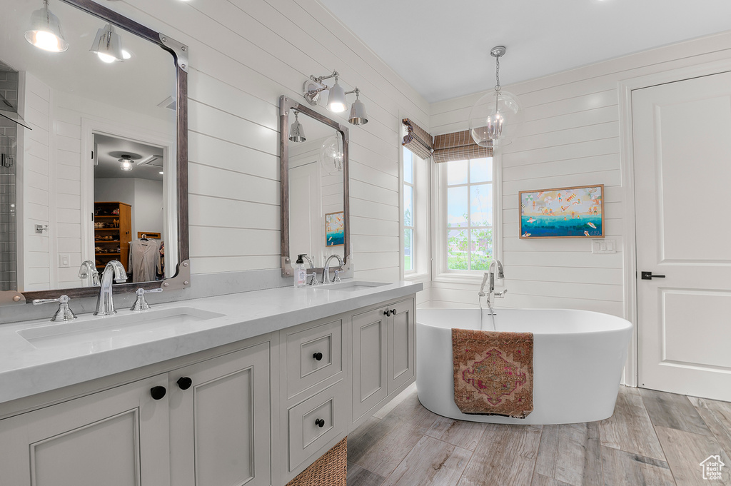 Full bath featuring a soaking tub, double vanity, wood finished floors, and wood walls