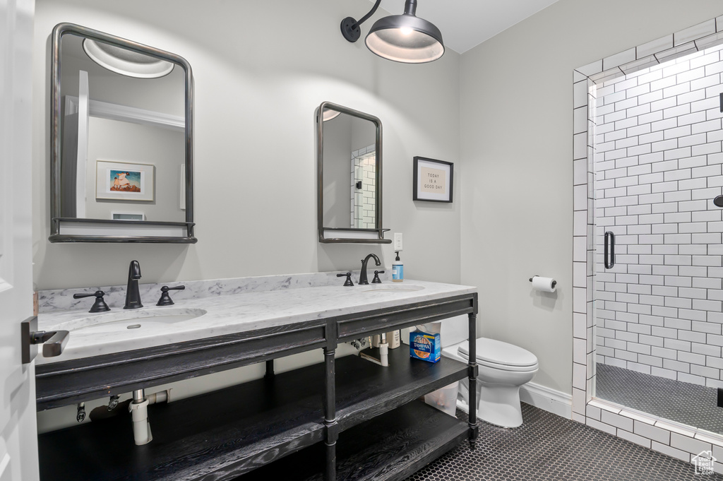 Bathroom featuring a shower stall, toilet, double vanity, and tile patterned flooring