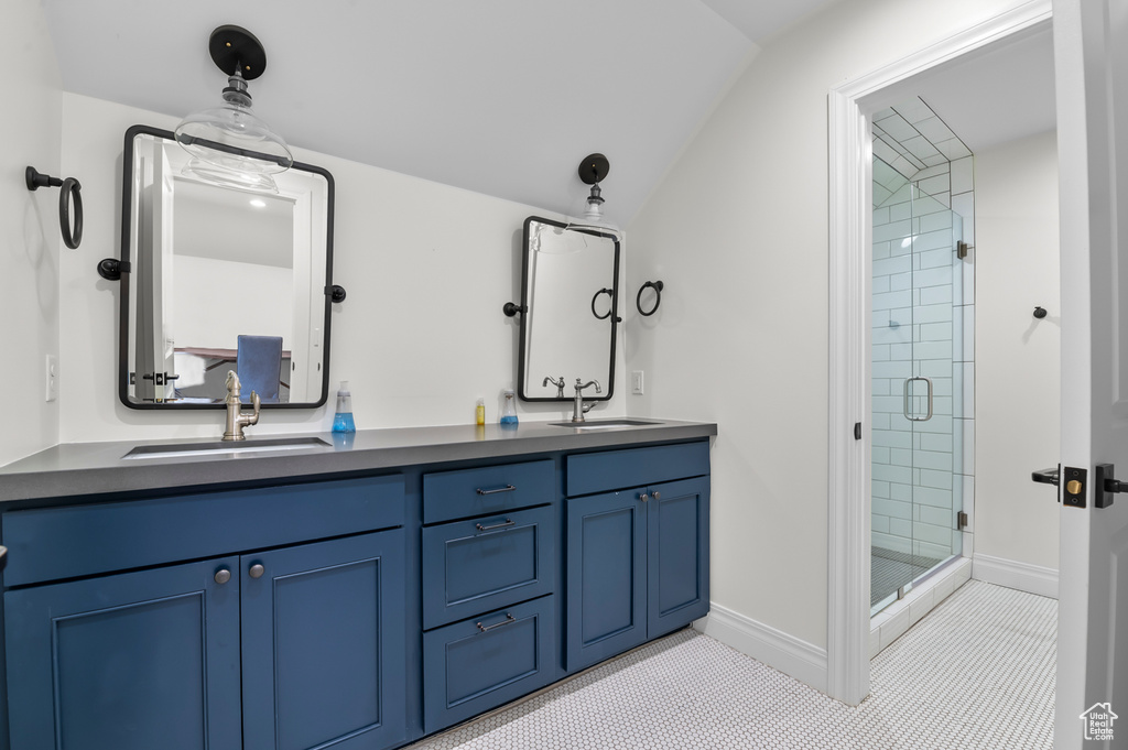 Full bath with a shower stall, double vanity, lofted ceiling, tile patterned flooring, and baseboards