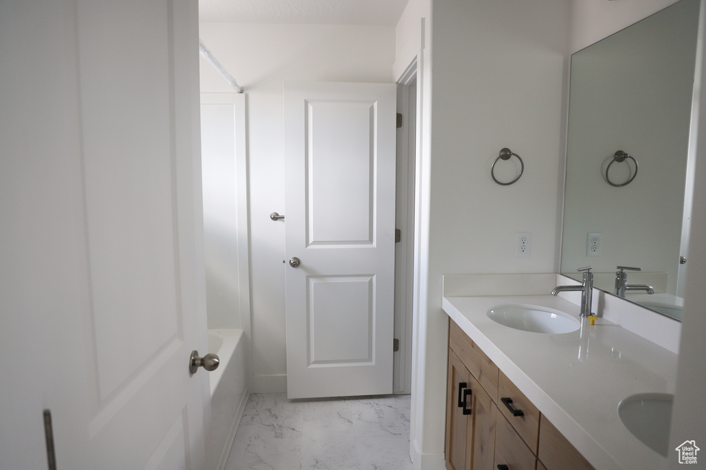 Full bathroom with marble look tiles, double vanity, and a tub